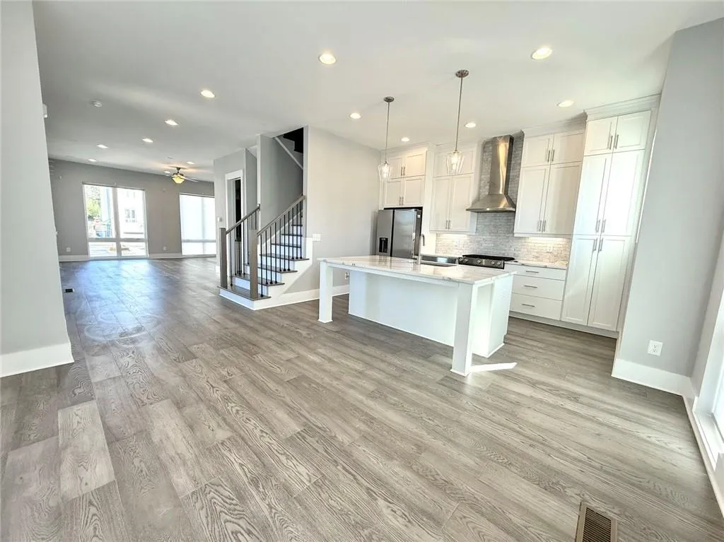 Kitchen with a sink, visible vents, light countertops, stainless steel refrigerator with ice dispenser, and wall chimney exhaust hood