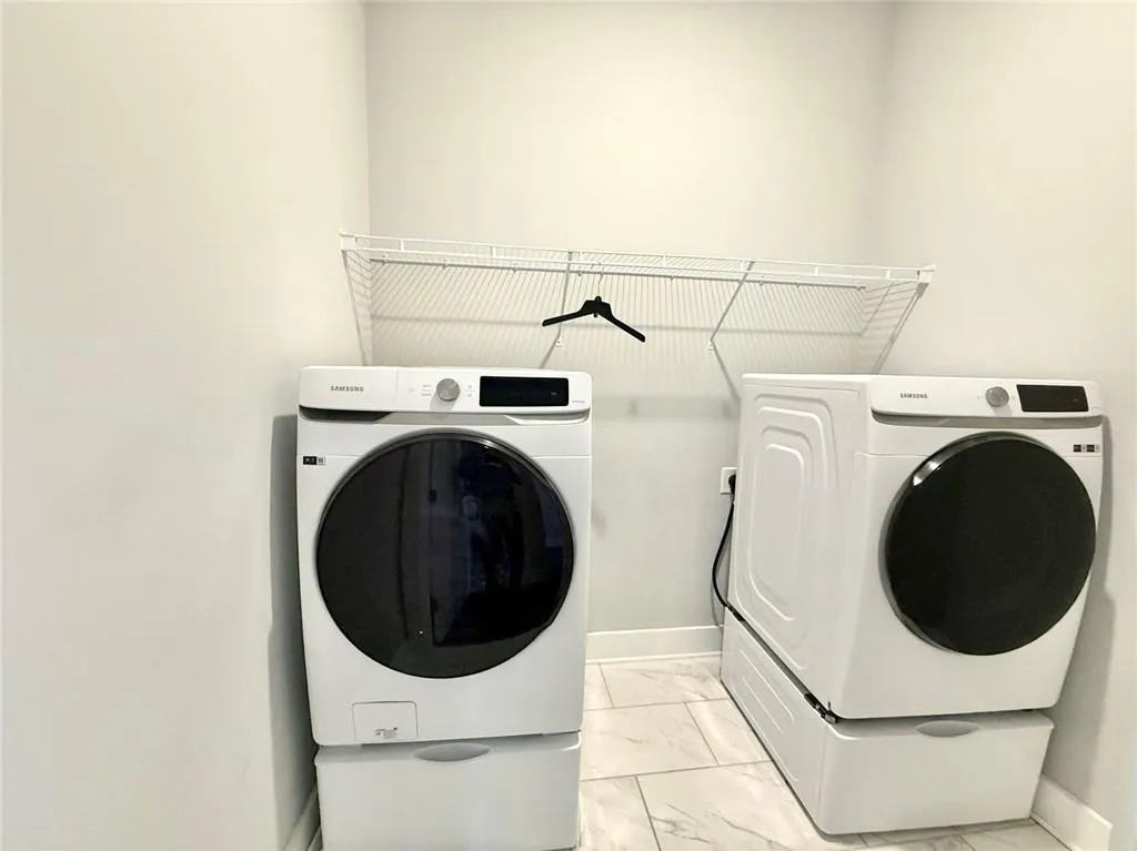 Clothes washing area featuring laundry area, independent washer and dryer, marble finish floor, and baseboards