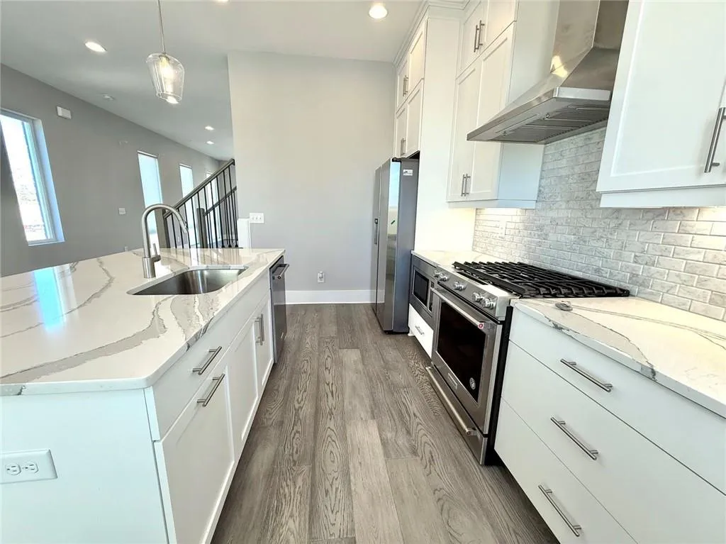 Kitchen featuring decorative backsplash, appliances with stainless steel finishes, white cabinets, a sink, and wall chimney exhaust hood