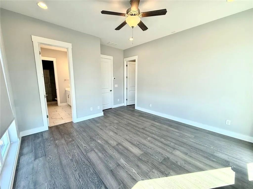 Unfurnished bedroom featuring visible vents, baseboards, a ceiling fan, dark wood-type flooring, and ensuite bathroom
