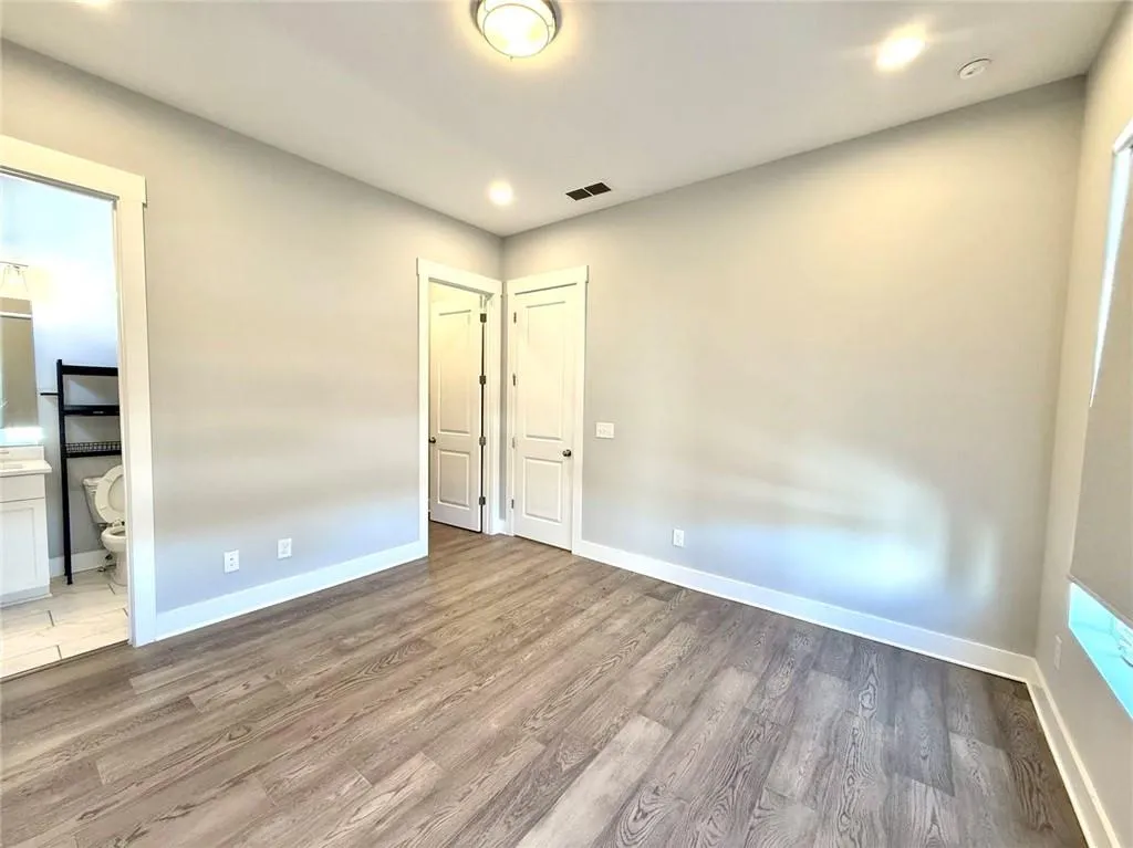 Unfurnished bedroom with ensuite bath, baseboards, visible vents, and wood finished floors