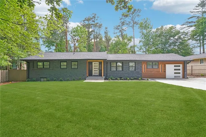 Contemporary ranch exterior featuring dark brick, wood paneling, a modern garage door, and a manicured lawn