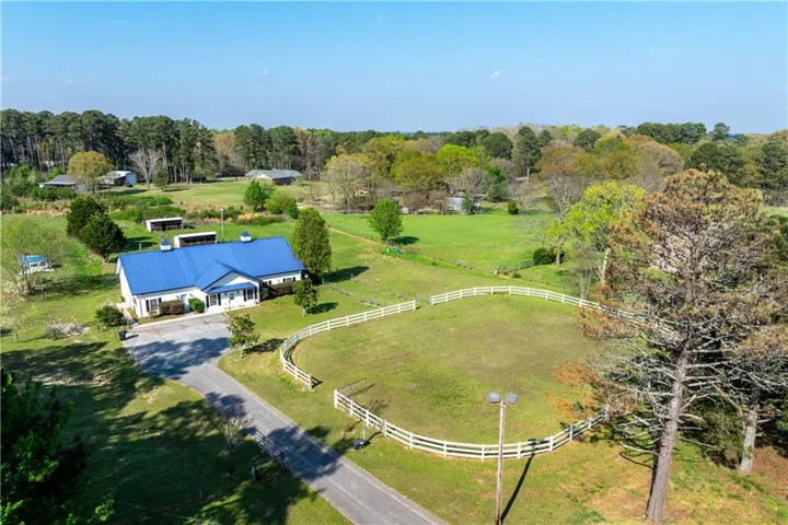Expansive green property featuring a white exterior home with a blue metal roof, a paved driveway, a fenced pasture, and mature trees