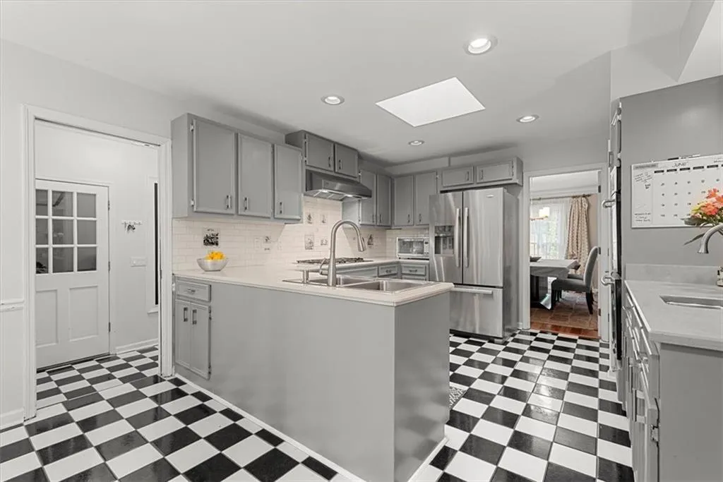 Kitchen featuring tasteful backsplash, tile floors, gray cabinetry, a skylight, and appliances with stainless steel finishes