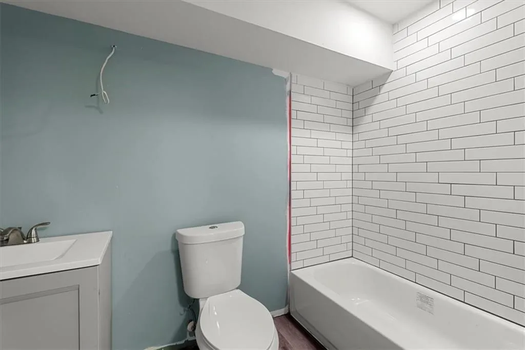 Full bathroom in basement with LVP flooring, vanity, toilet, and tiled shower / bath combo