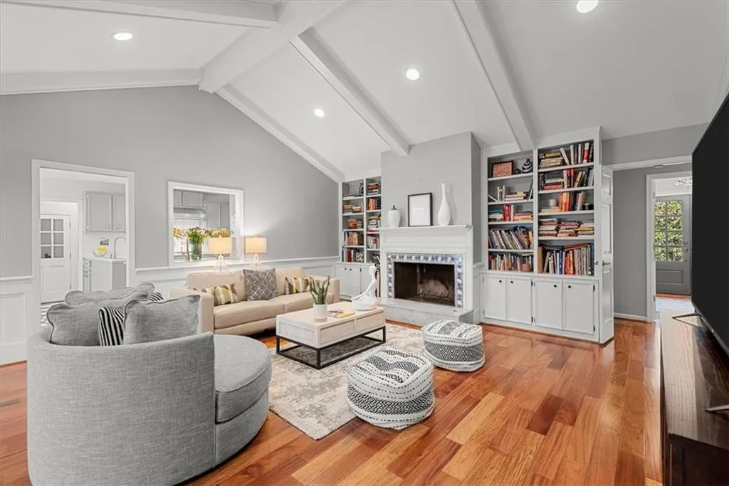 Living room with high vaulted ceiling, built in bookshelves, beam ceiling, and hardwood flooring