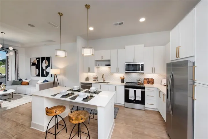 Kitchen featuring stainless steel appliances, open floor plan, decorative light fixtures, white cabinetry, and a kitchen bar