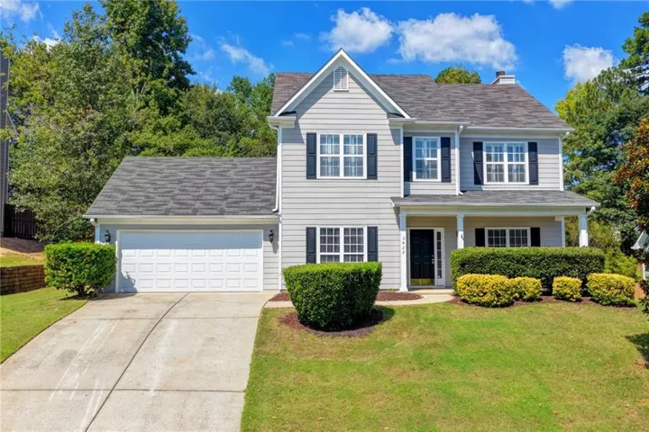 Two-story residence featuring light gray siding with contrasting black shutters, an integrated garage, a covered front porch, and a well-maintained lawn with mature landscaping