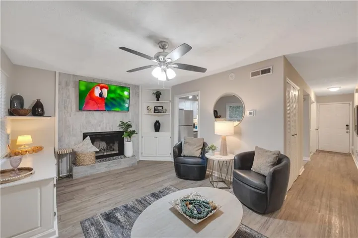 Living room with a textured ceiling, light wood-type flooring, a large fireplace, and ceiling fan