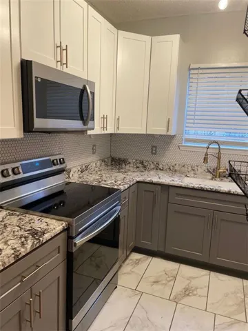 Kitchen featuring two-tone cabinetry, patterned countertops, stainless steel appliances, a white hexagon tile backsplash, and light-toned floor tiling