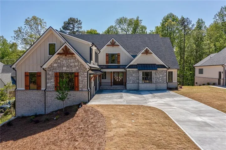 Craftsman-style house with board and batten siding, roof with shingles, stone siding, and concrete driveway