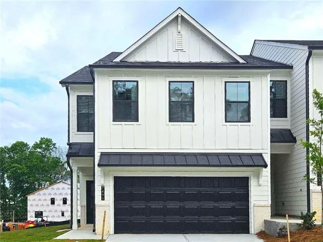 Modern farmhouse exterior featuring white board and batten siding, black framed windows, a black garage door, a black metal awning, and dark shingle roofing