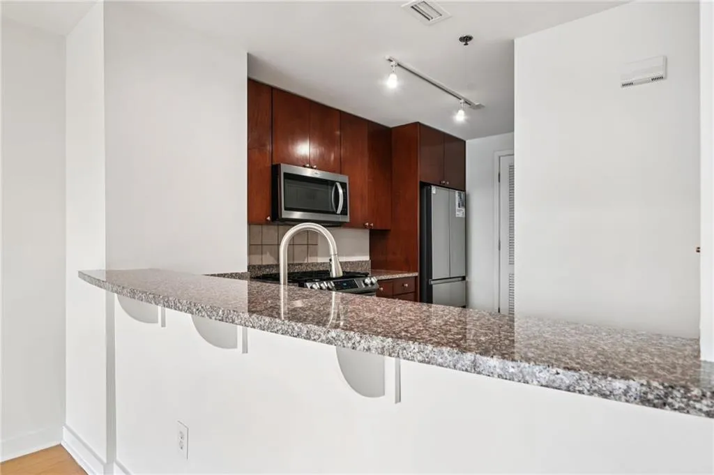 Kitchen featuring appliances with stainless steel finishes, a peninsula, dark stone countertops, a breakfast bar, and track lighting