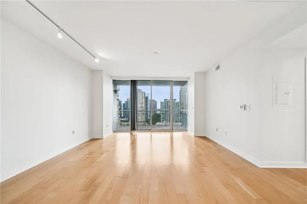 Empty room with floor to ceiling windows, a skyline view, rail lighting, light wood-style floors, and electric panel
