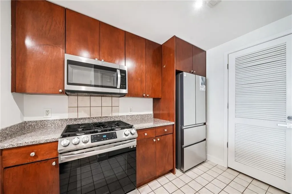 Kitchen with appliances with stainless steel finishes, light tile patterned floors, light stone countertops, and tasteful backsplash