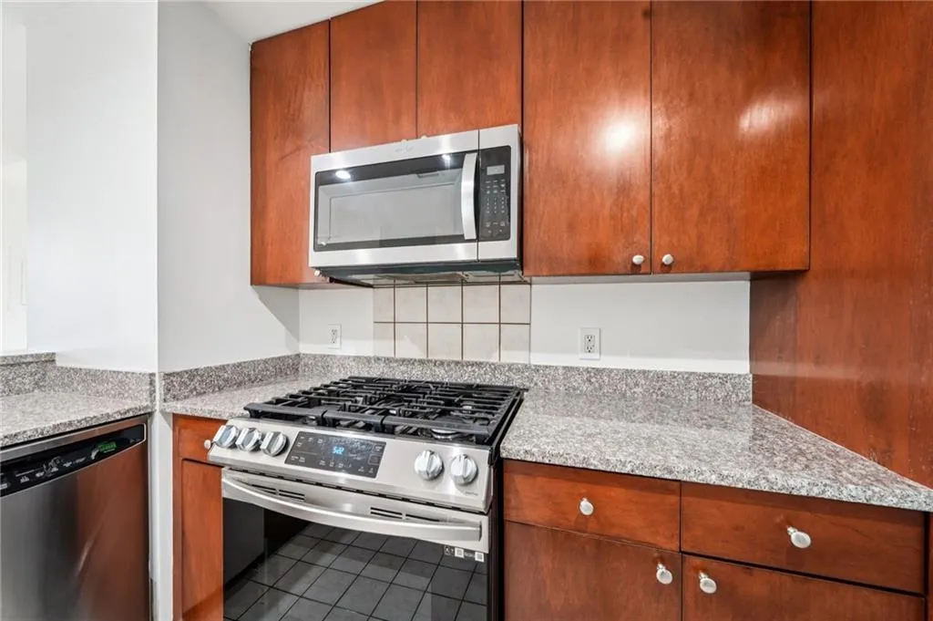 Kitchen with appliances with stainless steel finishes, light stone countertops, tile patterned flooring, and brown cabinets