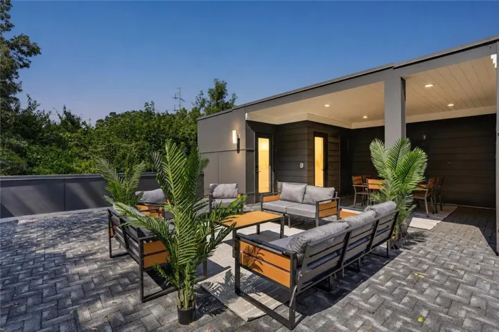 Expansive outdoor patio featuring herringbone paver flooring, a covered dining area with recessed lighting, and modern exterior wall sconces