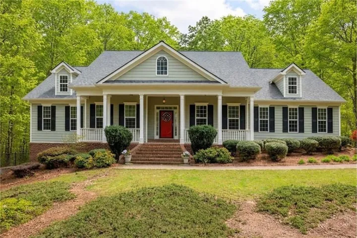 Traditional-style residence with a prominent covered porch, red entry door, and dormer windows