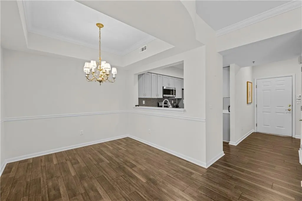 Unfurnished dining area featuring dark wood finished floors, a notable chandelier, baseboards, and a tray ceiling