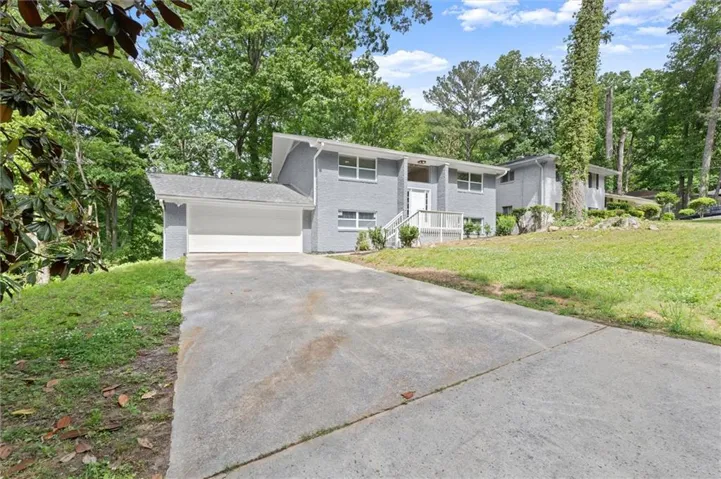 Split-level residence featuring a gray exterior finish, an attached two-car garage, and a front entry with white railings