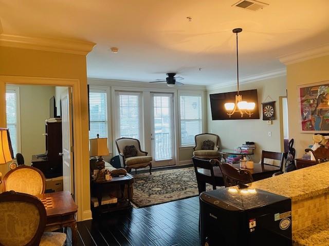 Living room featuring plenty of natural light, ceiling fan with notable chandelier, crown molding, and dark hardwood / wood-style flooring