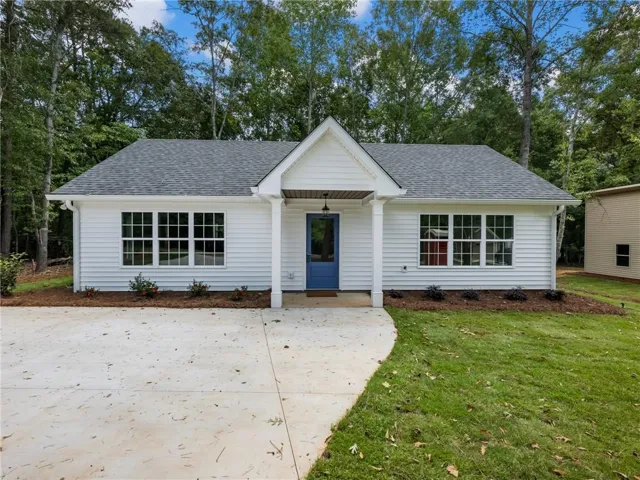 View of front facade with a porch, a shingled roof, a front lawn, and view of wooded area