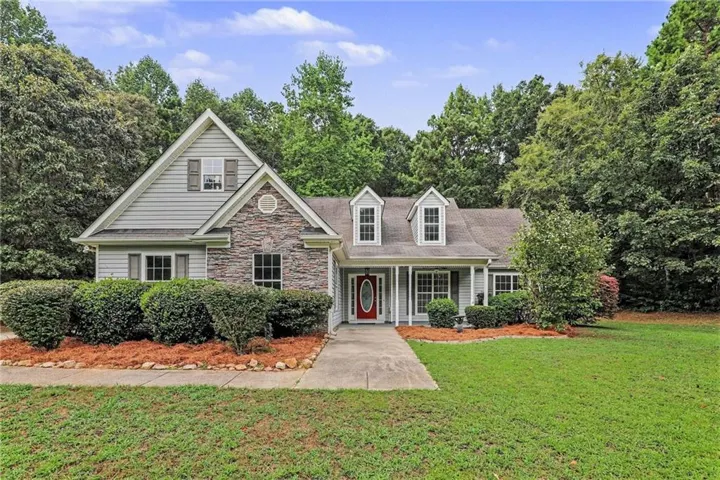 Exterior featuring stone accents, vinyl siding, a red entry door, dormer windows, and a paved walkway