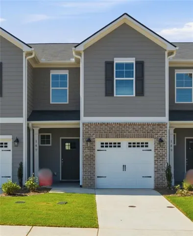 Contemporary townhome exterior featuring gray siding, a brick facade, white garage door with decorative hardware, and a neatly manicured lawn