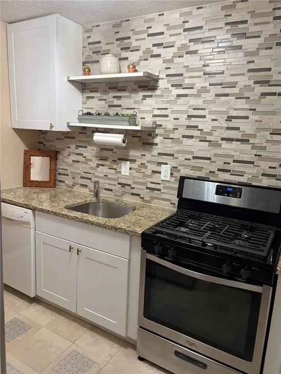 Kitchen with stainless steel gas range, light stone counters, white cabinets, dishwasher, and a textured ceiling