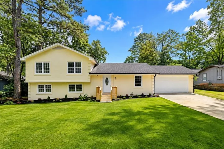 Bright exterior with a two-car garage, manicured lawn, and a paved driveway