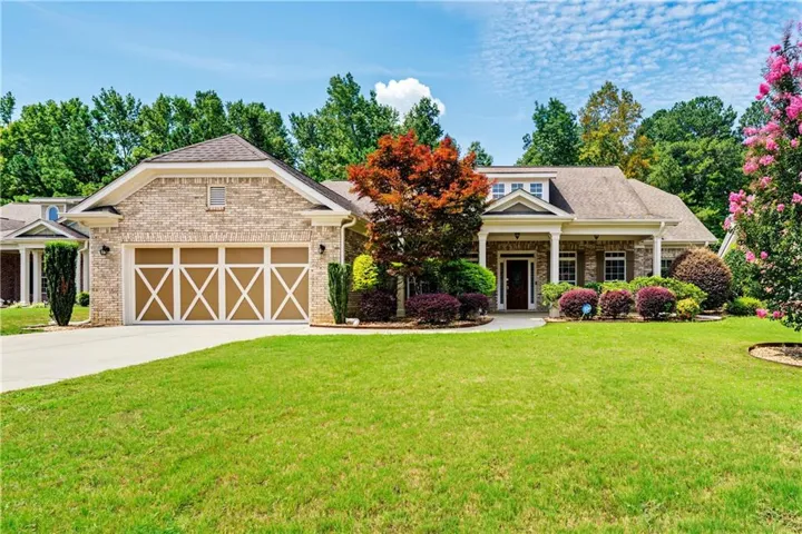 Brick exterior with a traditional roofline, mature landscaping, covered front entry, and a multi-car garage with decorative doors