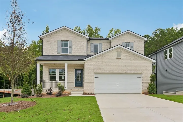 Two-story residence featuring light-colored brick siding, a covered front porch, and a two-car garage with a concrete driveway