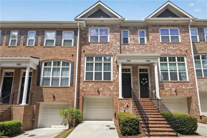 Brick townhome exterior featuring an arched window, white garage doors, and a covered entry with columns and railings