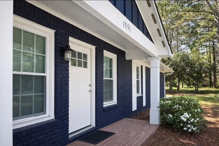 Brick exterior with white trim, front porch with brick pavers, white front door with glass panels, white-framed windows, and a decorative outdoor light fixture