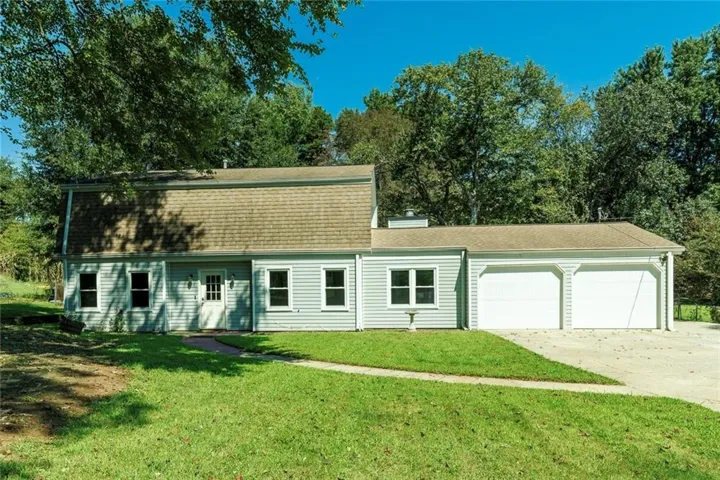 Light-toned siding exterior with multiple windows, a gambrel roof, and an attached two-car garage