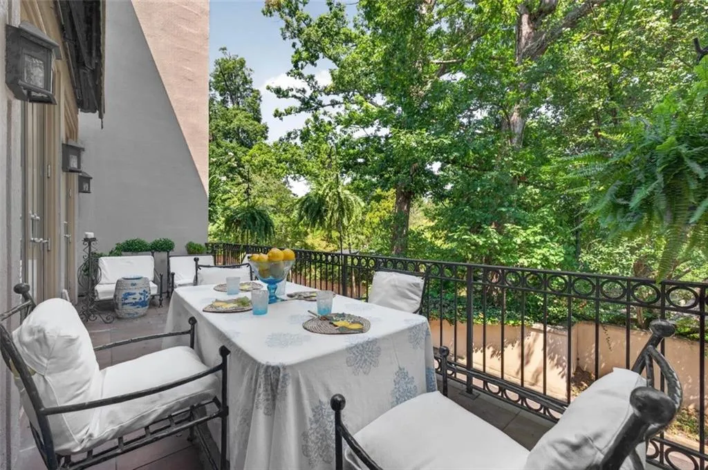 Outdoor balcony featuring an ornate black metal railing, a paved surface, and lush perimeter trees