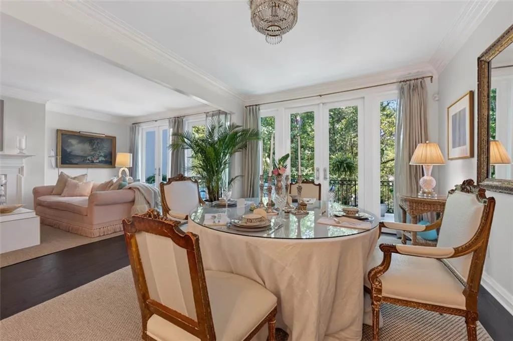 Glass-top dining table, French doors with balcony access, wood-finish flooring, white crown molding, and ornate chandelier