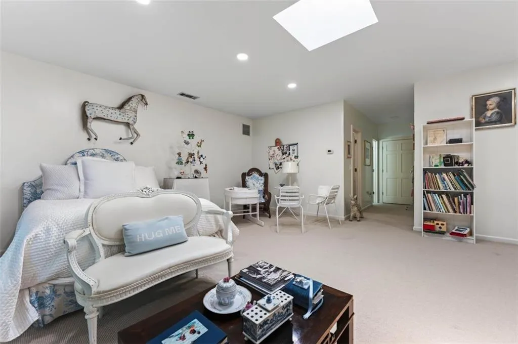 Recessed lighting and skylight illuminate a spacious room featuring wall-to-wall carpeting and a built-in bookshelf
