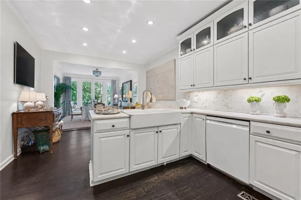 White cabinetry with dark hardware, white farmhouse sink, white countertops, white tile backsplash, and dark wood-finish flooring
