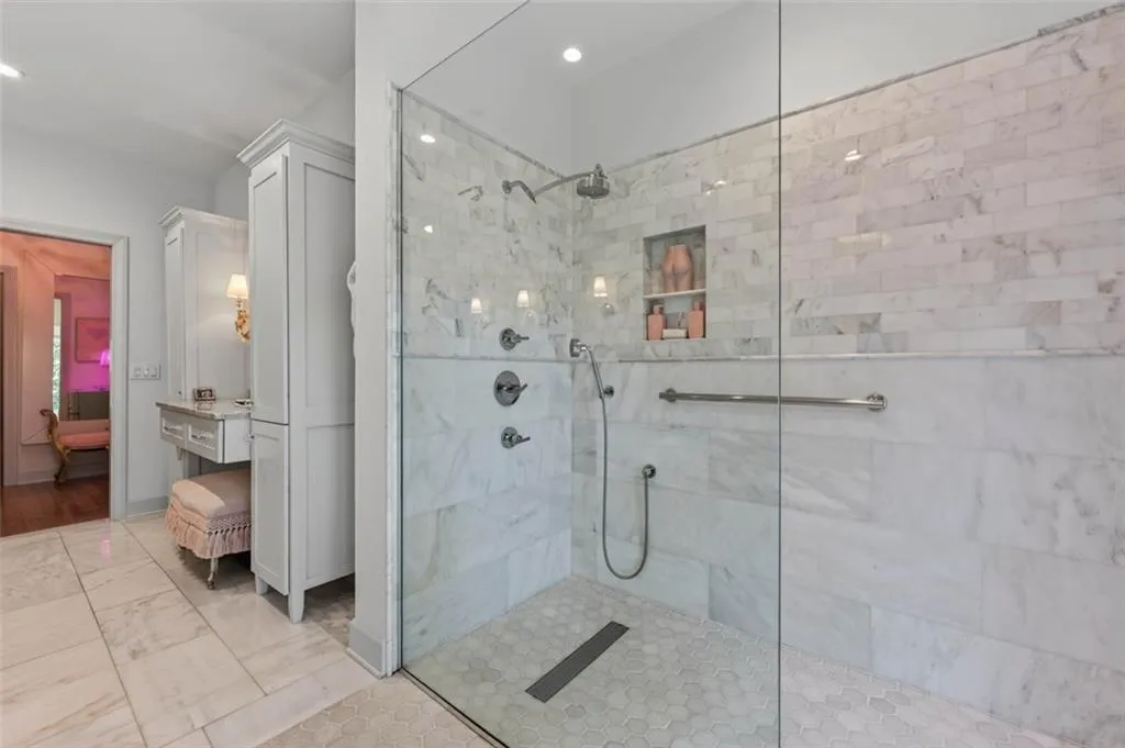 Glass-enclosed shower with a rainfall showerhead, handheld shower fixture, and built-in niche