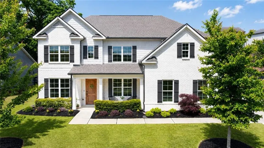 White brick exterior with dark shutters, gabled rooflines, covered porch, wood-finish front door, and manicured landscaping