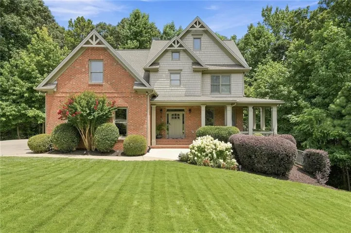 Two-story residence featuring a brick and shake exterior, a covered front porch, and dormer windows