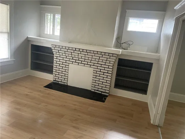Fireplace featuring white brick with dark grout, built-in shelving, wood-finish flooring, and white trim