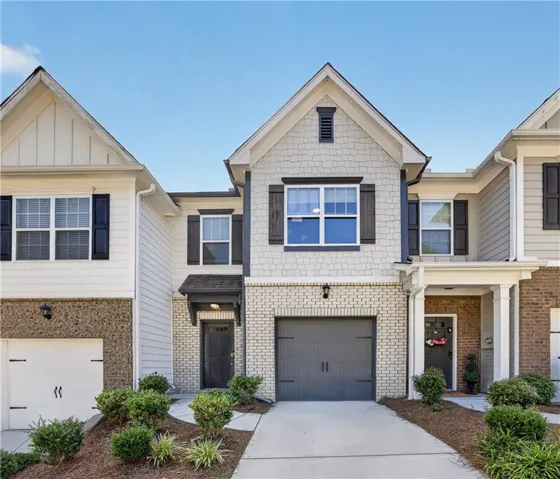 Contemporary townhouse exterior featuring a gabled roofline, light-colored brick, shake siding, and a single-car garage with a dark gray door
