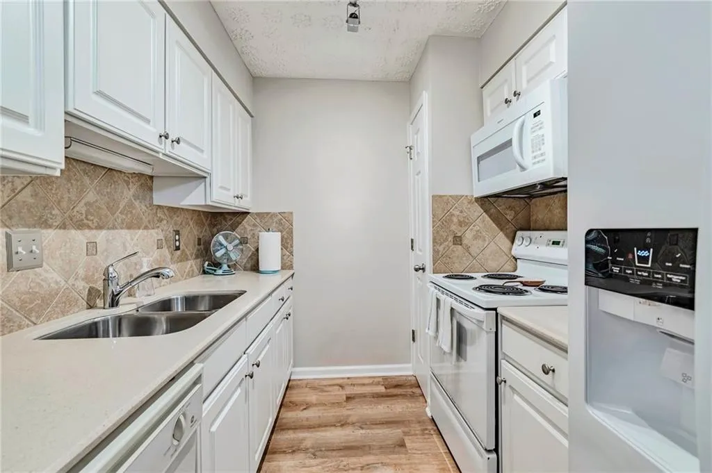 Kitchen featuring white cabinetry, light countertops, tasteful backsplash, white appliances, and light wood finished floors.