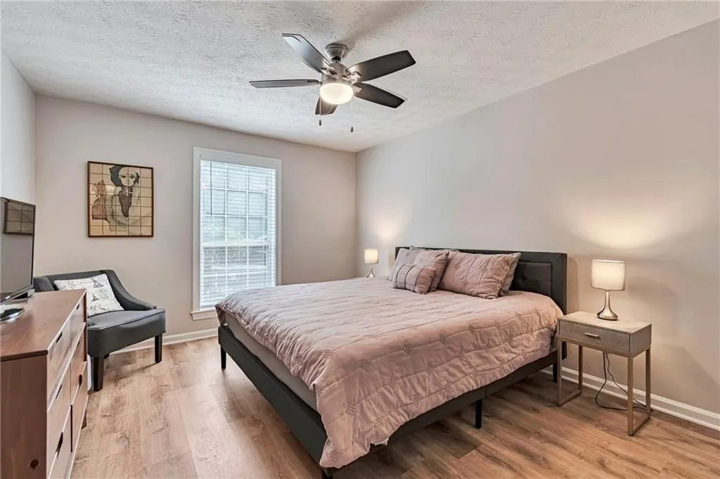 Bedroom large enough for King Bed featuring picture window, ceiling fan, and light wood finished floors.