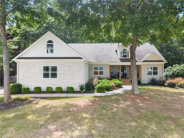 Cottage-style home featuring a white brick and horizontal siding exterior, a covered front porch with wood-finish columns, a curved concrete walkway, and established landscaping