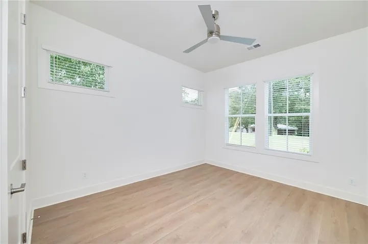 Wood-finish flooring, multiple windows with blinds, and a ceiling fan with integrated lighting