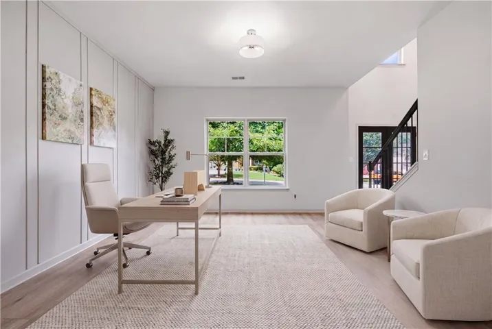 Wood-finish flooring with a light-toned area rug, a window providing natural light, and a staircase with a dark-finish railing