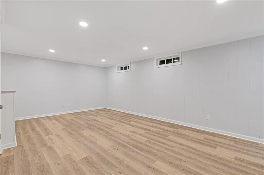 Finished basement featuring light wood finished floors, crown molding, recessed lighting, and wood walls
